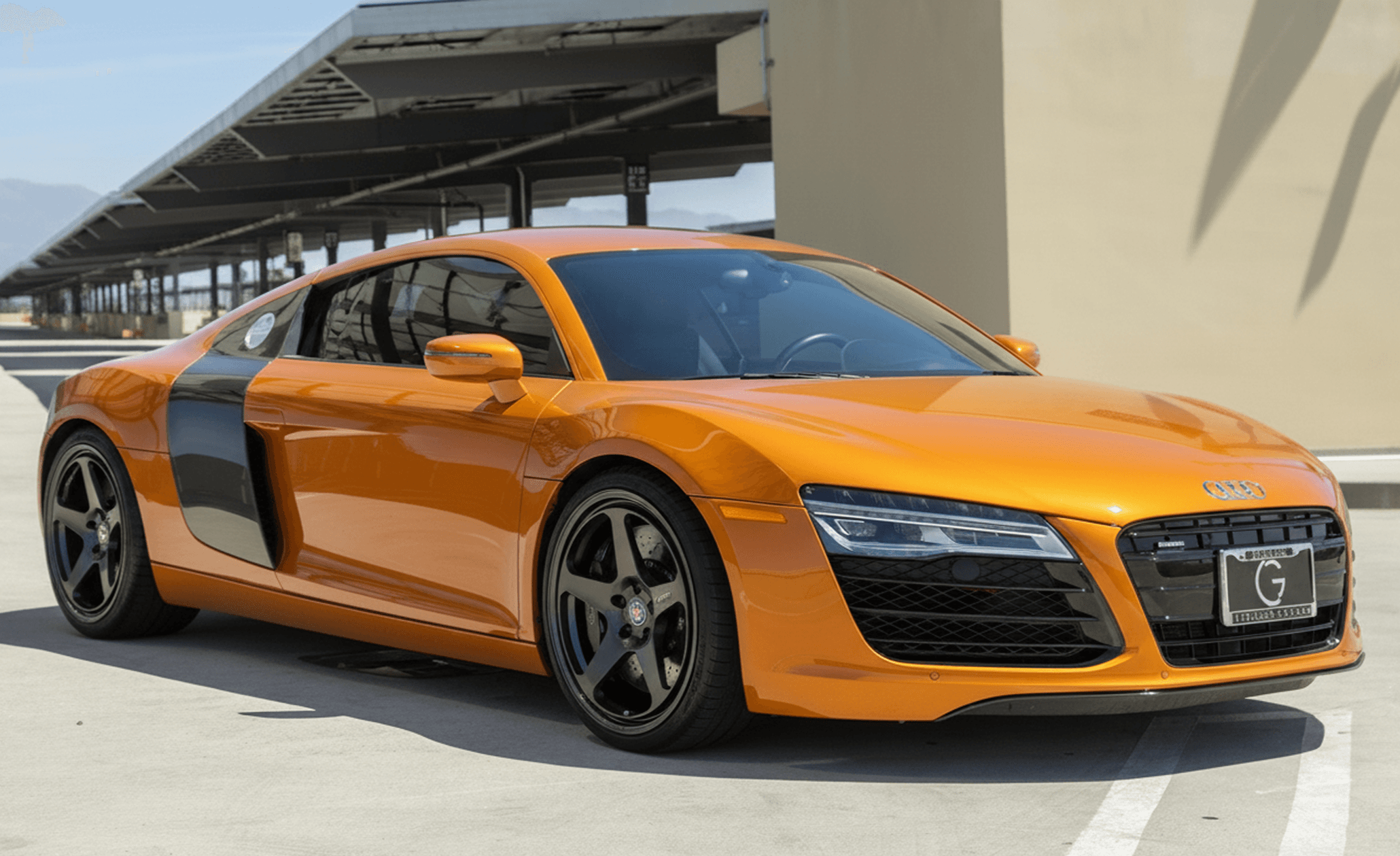 Orange Audi R8 (first gen) front three‑quarter with carbon side blade in a parking structure