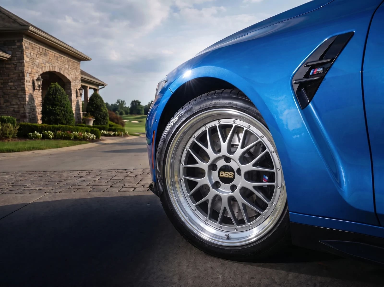 Blue BMW M4 close-up with polished BBS LM silver wheels outside a stone home