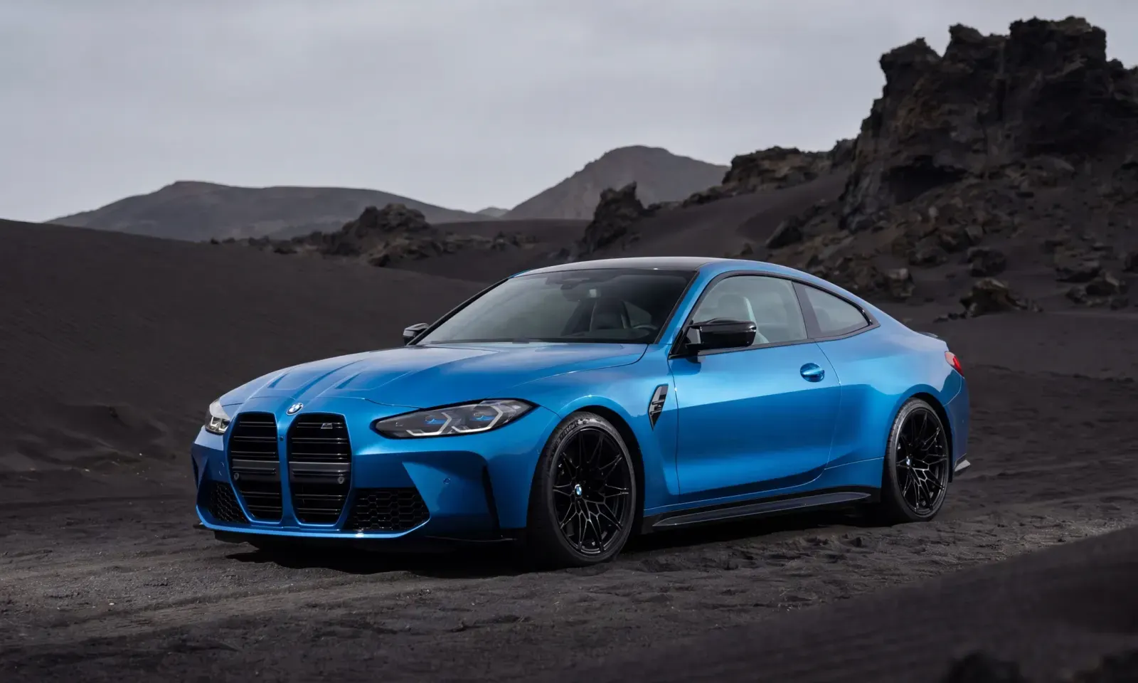 Blue BMW M4 coupe on black volcanic sand with dark factory wheels