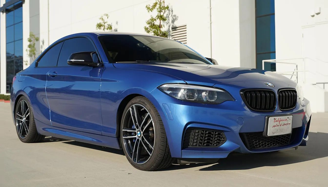 Blue BMW 2 Series coupe with factory wheels parked outside a modern building